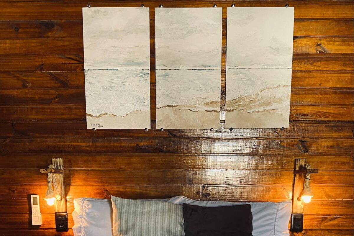 A wooden-paneled room with a bed, two wall-mounted lamps, and a painting above the bed.