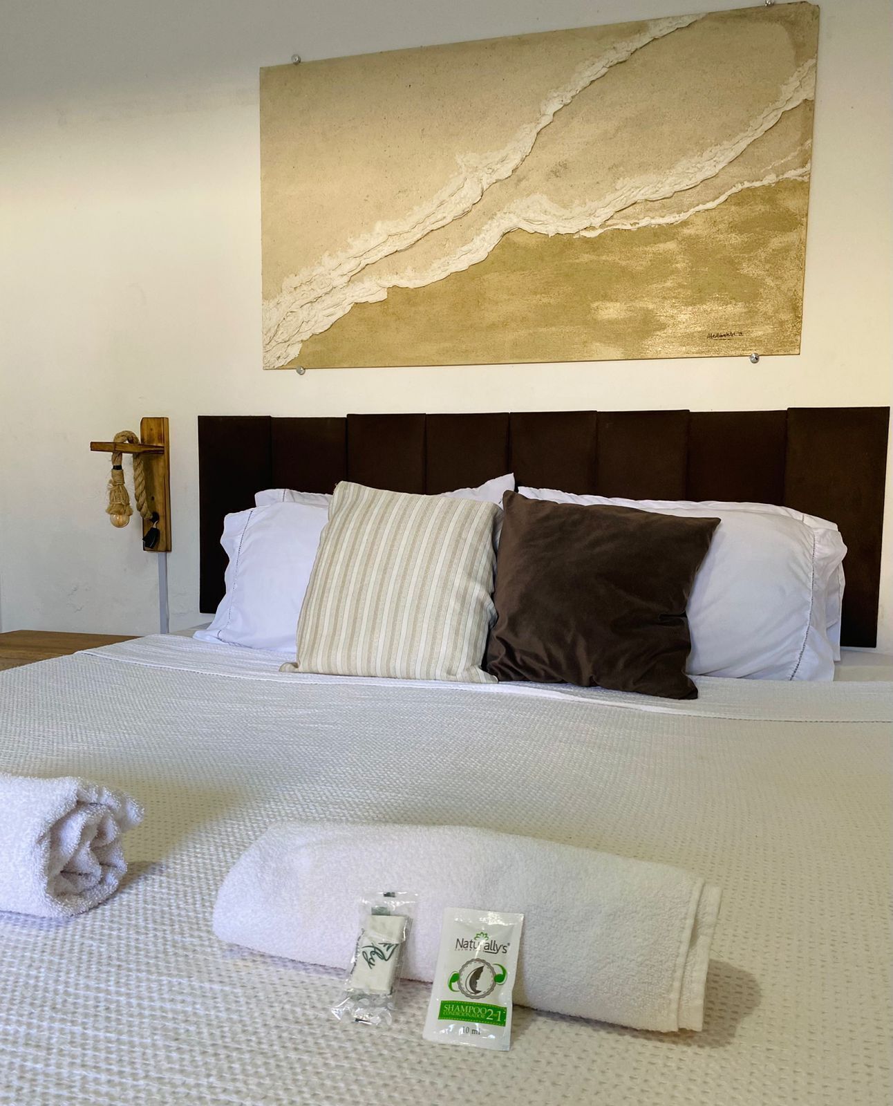 A neatly made bed with white linens, a striped pillow, and a brown pillow. There are two bottles of shampoo on the bed.
