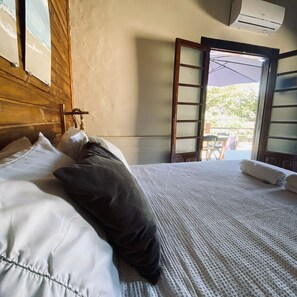 A bed with white and dark pillows, a wooden headboard, and a window with a view of the outdoors. - Encanto Paraty Beach (Paraty)