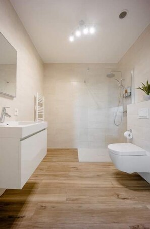 A modern bathroom with a wooden floor, a white sink, a toilet, and a shower area. - New building, 500Mbps, Parking, A+ Location (Luxembourg)