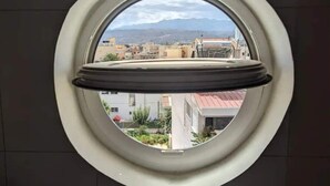 A round window with a view of a cityscape and mountains in the distance. - 5th-Floor Cozy Sea View, 2-Min Beach Walk (Chania)