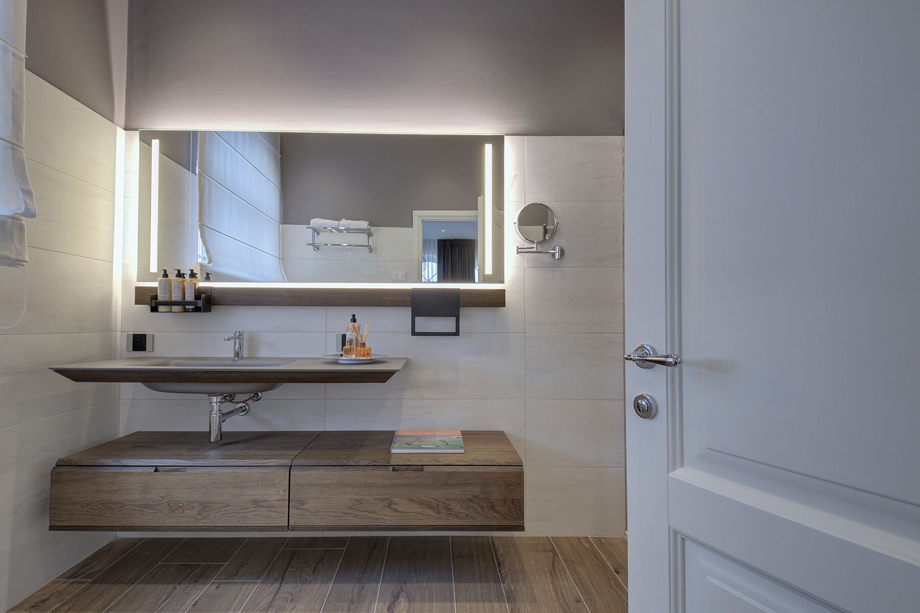 A modern bathroom with a wooden vanity, a large mirror, and a built-in sink.