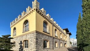 Un edificio storico con facciata gialla e base in pietra, caratterizzato da finestre ad arco e un cortile in pietra.