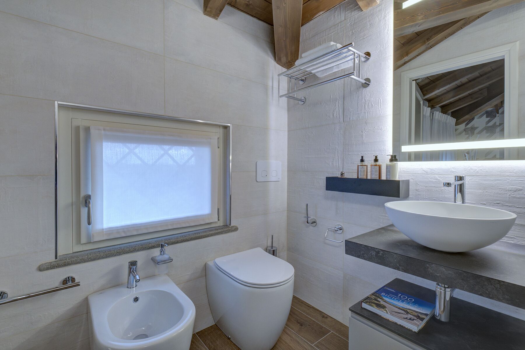 A bathroom with a bidet, toilet, vanity with a large sink, and a window.