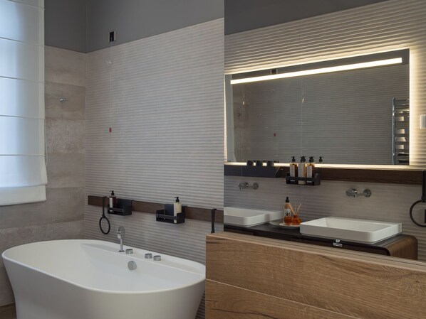 Un baño moderno con una bañera independiente, dos lavamanos con espejos y un mueble-lavabo con encimera de madera.