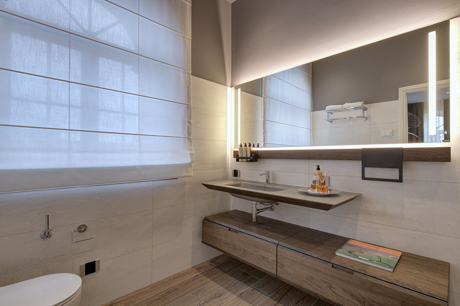 A modern bathroom with a large mirror, a wooden vanity, a sink, and a toilet.