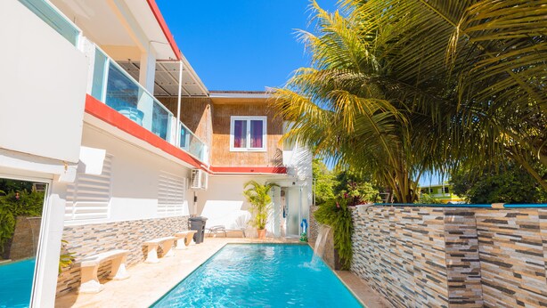 A swimming pool with a stone wall and palm trees, surrounded by a building with a red roof and a window. - Vacation House With Private Pool Bambam 2 (Aguada)