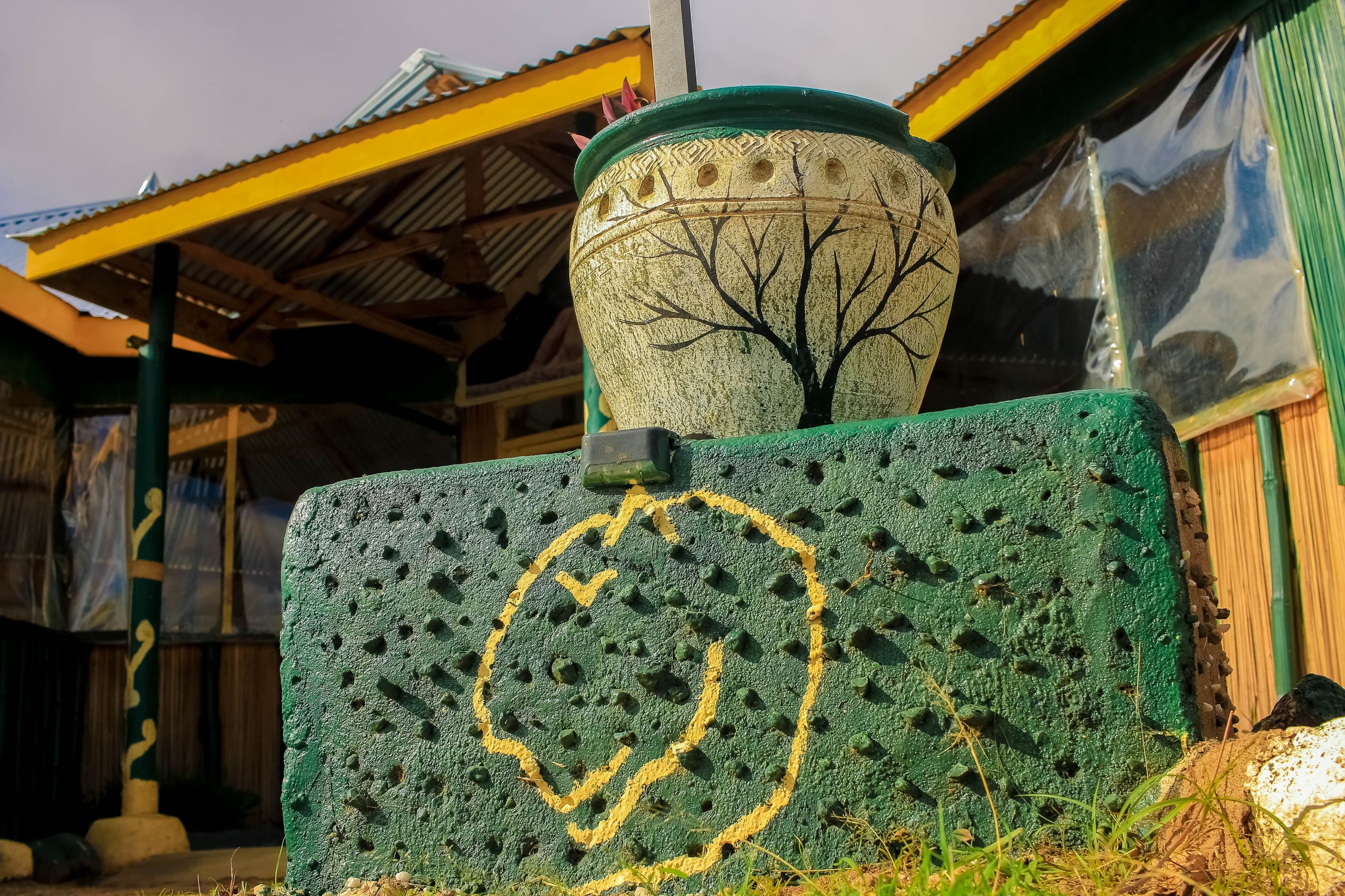 Pared verde con textura, un diseño circular amarillo y una maceta decorativa con un motivo de árbol.