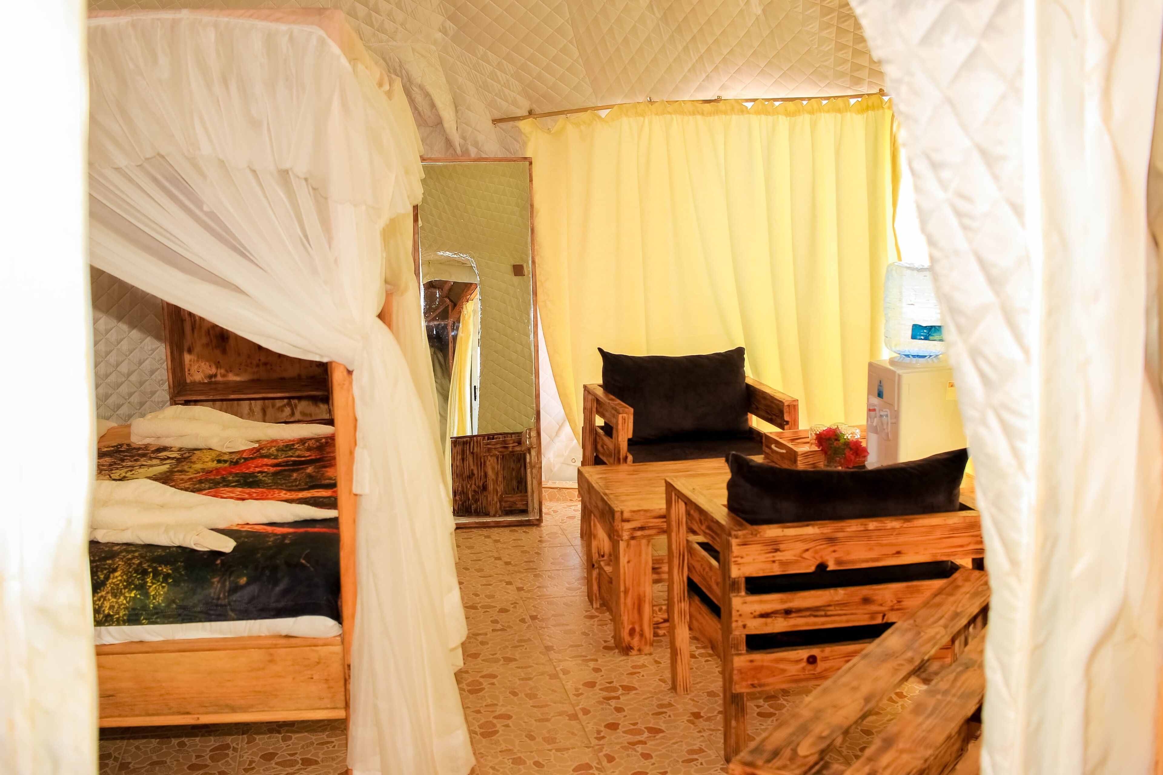Une pièce avec un lit recouvert de draps blancs, un banc en bois et une table sur laquelle repose un coussin noir.