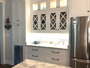 Una cocina con armarios blancos, un refrigerador de acero inoxidable y una encimera de mármol.