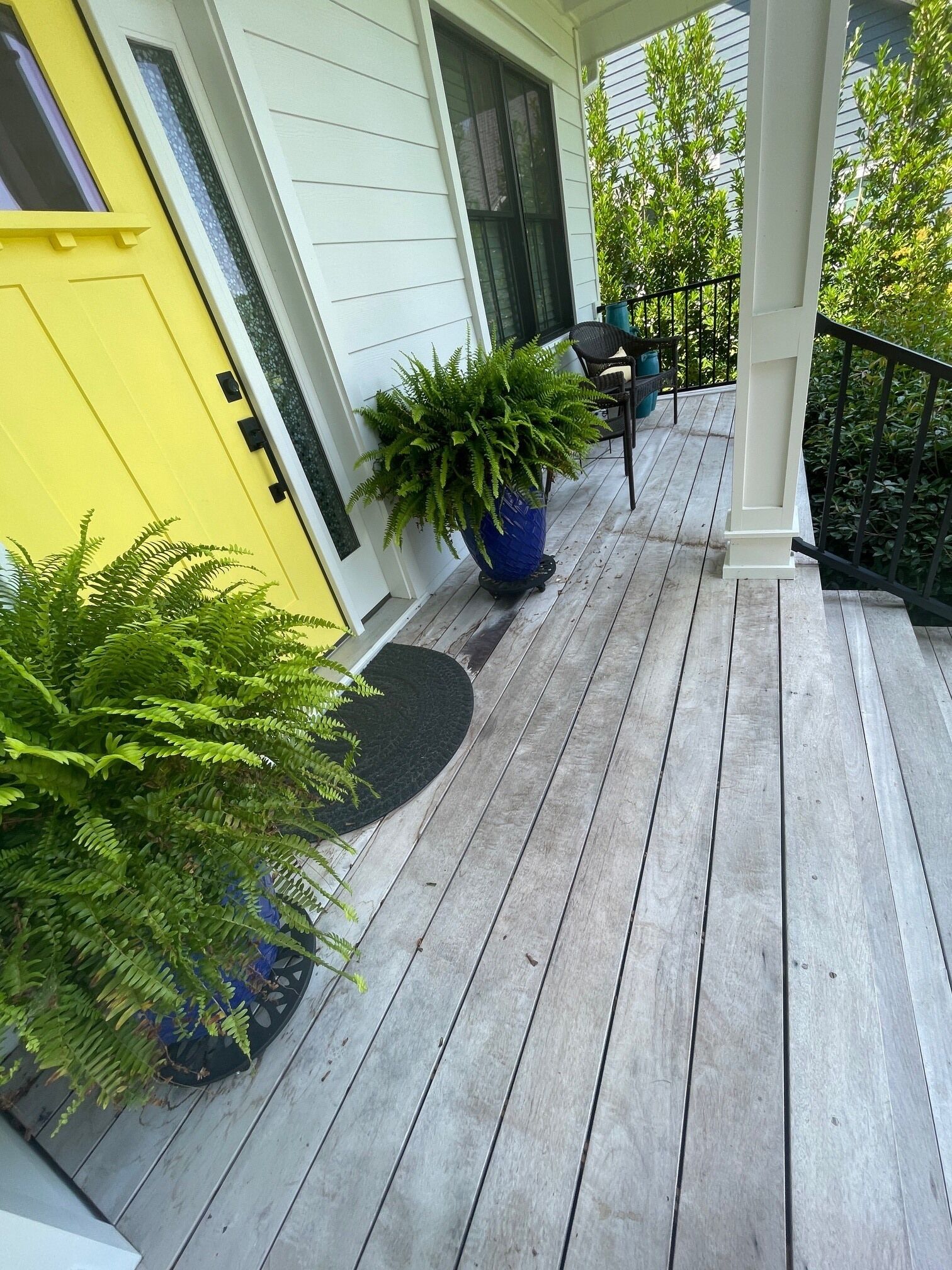 A wooden porch with a yellow door, a potted plant, and a chair.