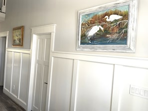 Un couloir avec des lambris blancs et deux œuvres d’art encadrées accrochées au mur.