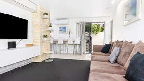 Un soggiorno moderno con TV a schermo piatto, una parete decorata in pietra, un divano con cuscini, un'area pranzo con sedie e vista panoramica tramite una porta in vetro.