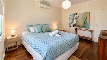 A bedroom with a bed, bedside tables, a nightstand, a lamp, a painting, a bench, and a door.