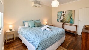 Une chambre à coucher comprenant un lit, des tables de chevet, une commode, une lampe, un tableau, un banc et une porte.
