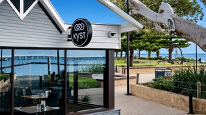A restaurant with a view of the water and a bridge, featuring a sign with the logo 'KYST'.