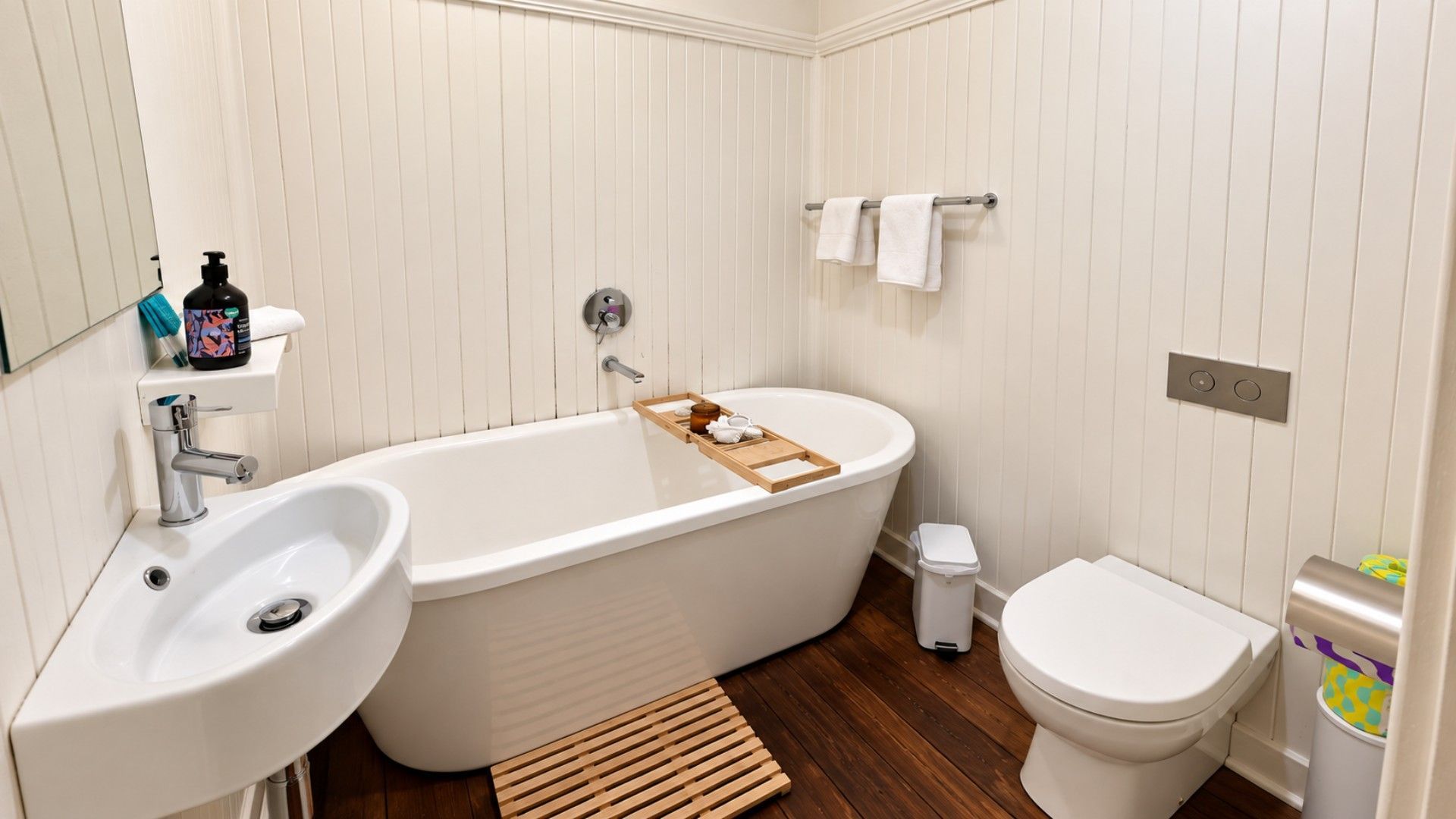 A bathroom with a bathtub, sink, toilet, and a wooden shelf with toiletries.