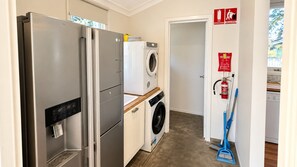 A compact kitchen with a stainless steel refrigerator, a washing machine, and a fire extinguisher on the wall. - Barefoot Beach Cottage (Geographe)