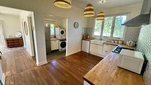 Una cocina con piso de madera, gabinetes blancos, horno empotrado y lámparas colgantes.