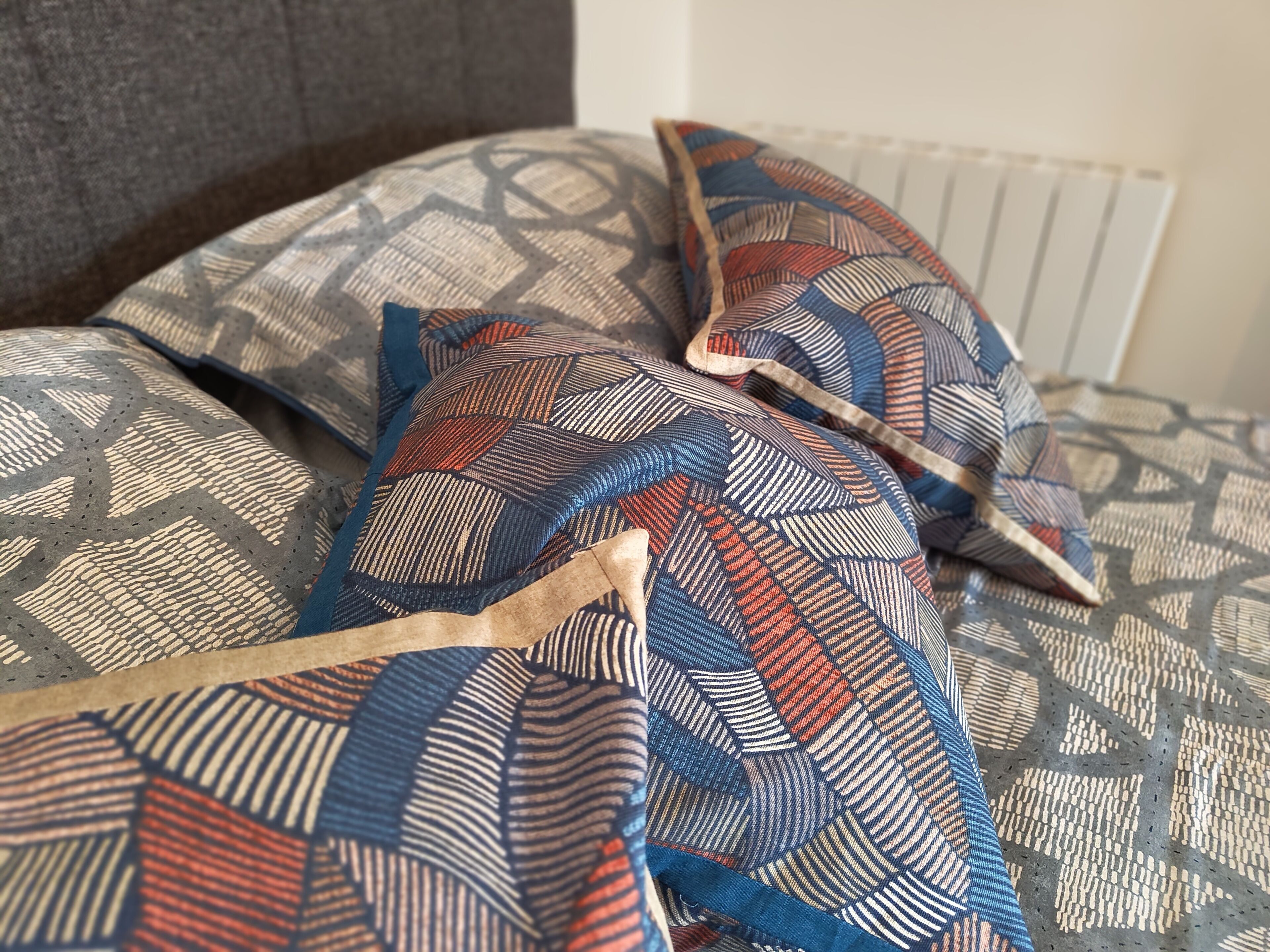 A bed with patterned pillows and a grey headboard.