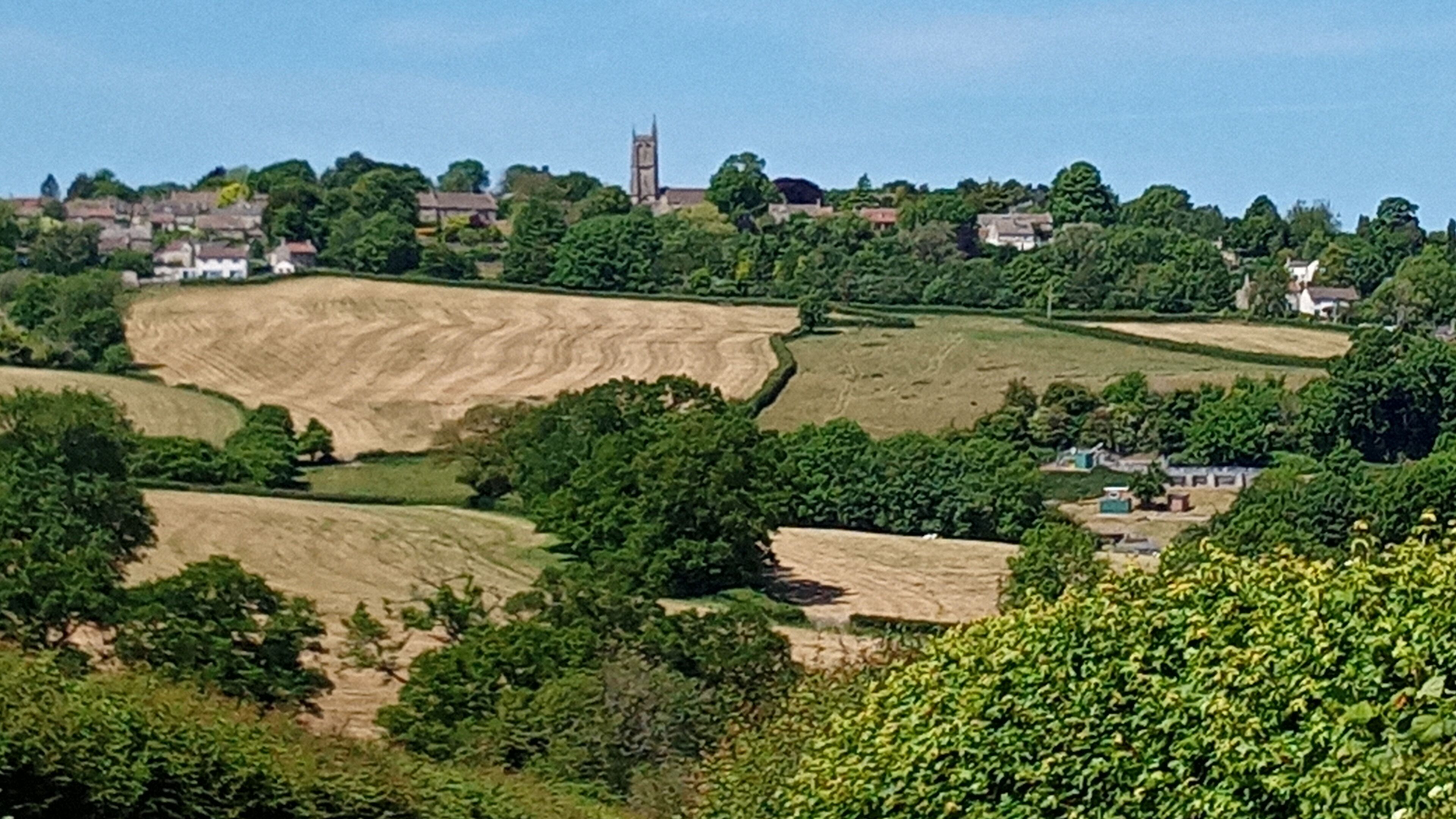 Un paysage rural caractérisé par des champs vallonnés, un clocher d’église et des maisons dispersées.