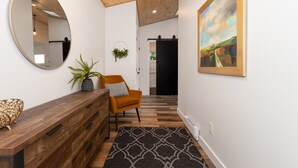 A hallway with a wooden ceiling, a round mirror, a potted plant, a sofa, a painting, and a patterned rug. - New Garden Studio I ProClean I Skylight I Rain Shower I Nespresso I Free Parking (Colwood)