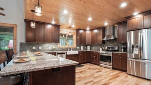 A modern kitchen with wooden cabinets, granite countertops, stainless steel appliances, and a large island with seating. - Hot Tub, Firepit, Large Deck, Game Room, Secluded Mtn Views, 20 min to Park | Yellowstone Escape (Island Park)