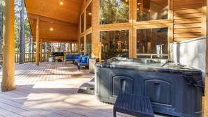 A wooden deck with a hot tub, outdoor seating, and large windows. - Hot Tub, Firepit, Large Deck, Game Room, Secluded Mtn Views, 20 min to Park | Yellowstone Escape (Island Park)