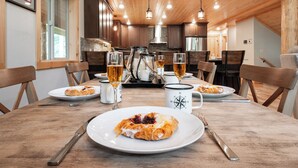 A dining area with a wooden table set for four, featuring plates of food, glasses of beer, and a coffee pot. - Hot Tub, Firepit, Large Deck, Game Room, Secluded Mtn Views, 20 min to Park | Yellowstone Escape (Island Park)