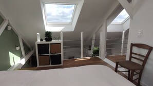 Een slaapkamer met dakraam, een bed, een houten stoel en een witte kledingkast met planken.