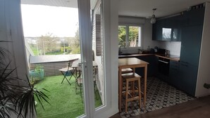 Een moderne keuken met een groot raam, een eethoek met tafel en stoelen, en een kleine buitenhofje zichtbaar door de glazen deur.