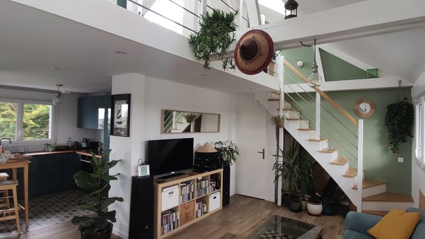 Een ruime woonruimte met een hoge plafond, een trap en een keuken op de achtergrond.