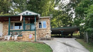 A stone house with a porch, a covered area, and a paved driveway.