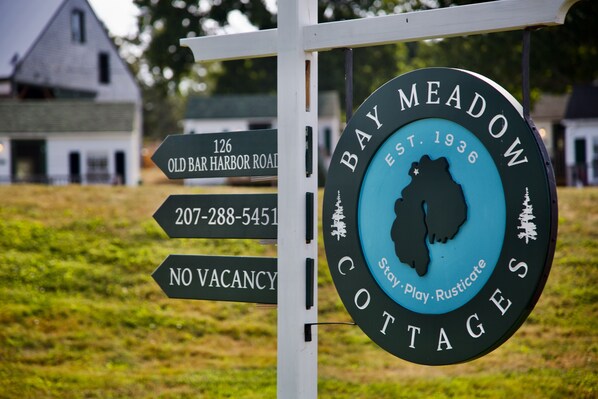 A sign for Bay Meadow Cottages with a silhouette of a cottage, a phone number, and a note stating no vacancies.