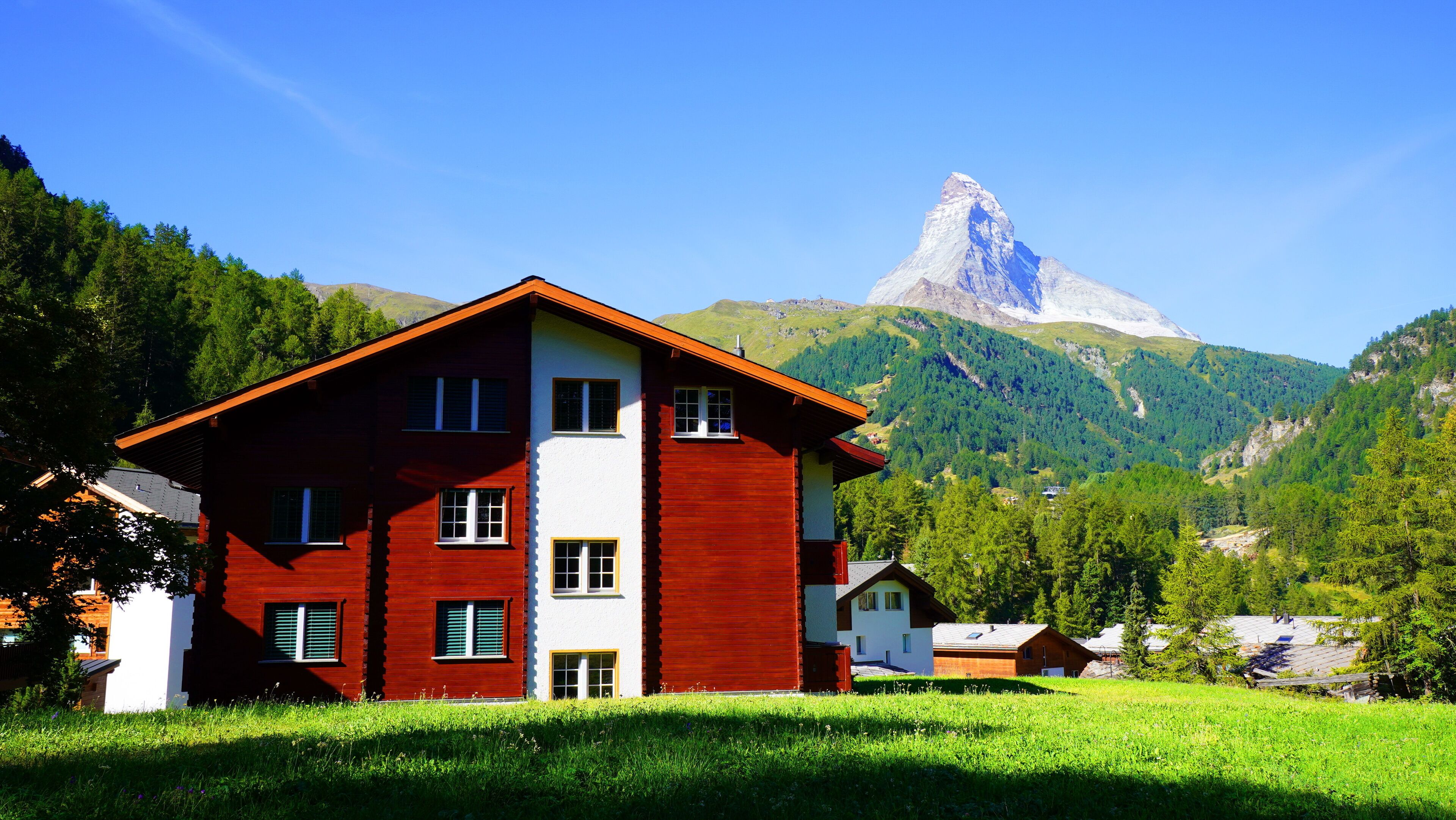 A two-story building with a red facade and white upper section, set against a mountainous backdrop.