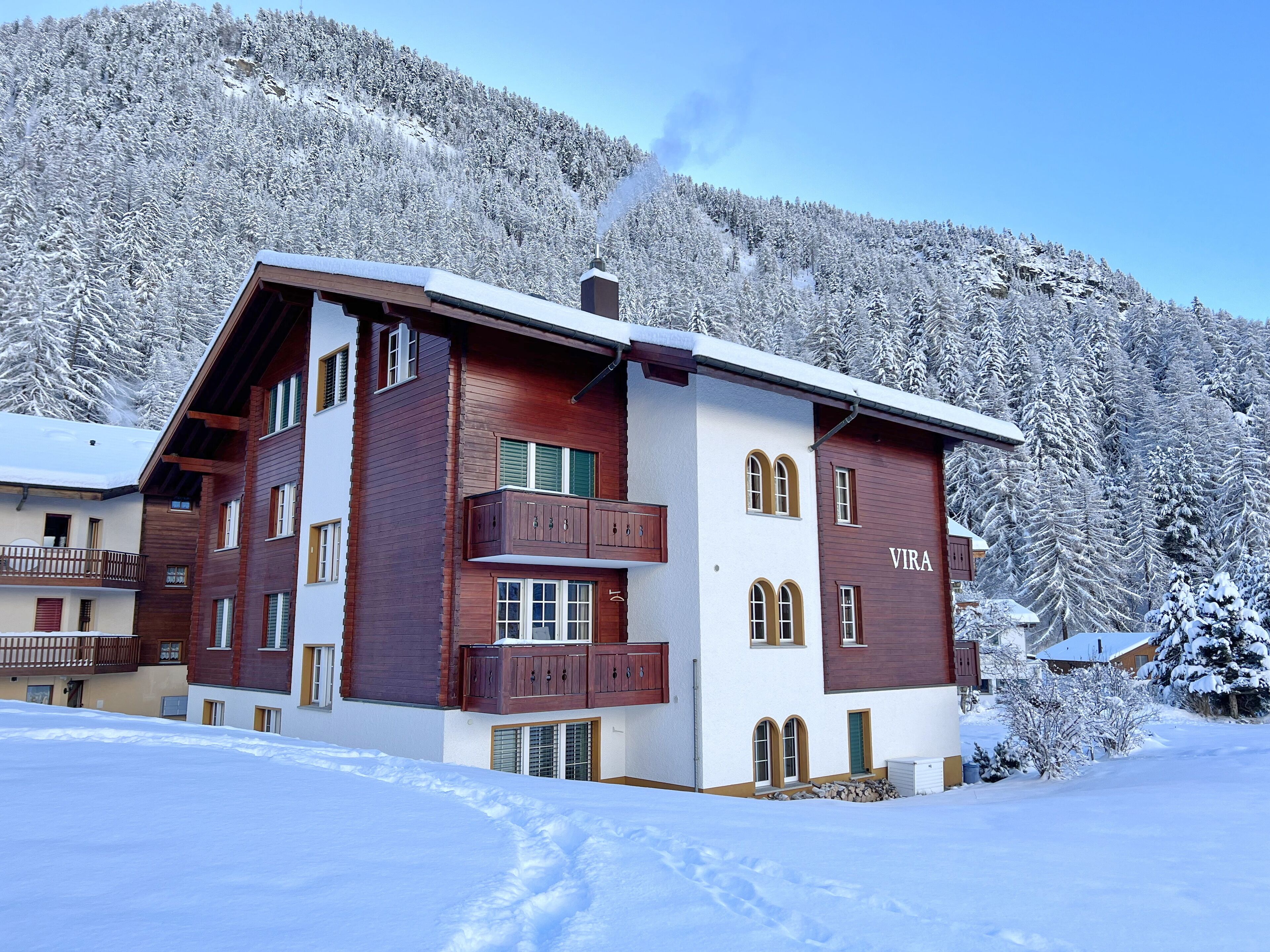 A multi-story chalet with a wooden facade, a balcony, and a nameplate reading "VIRA".