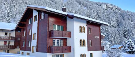 A multi-story chalet with a wooden facade, a balcony, and a nameplate reading "VIRA".