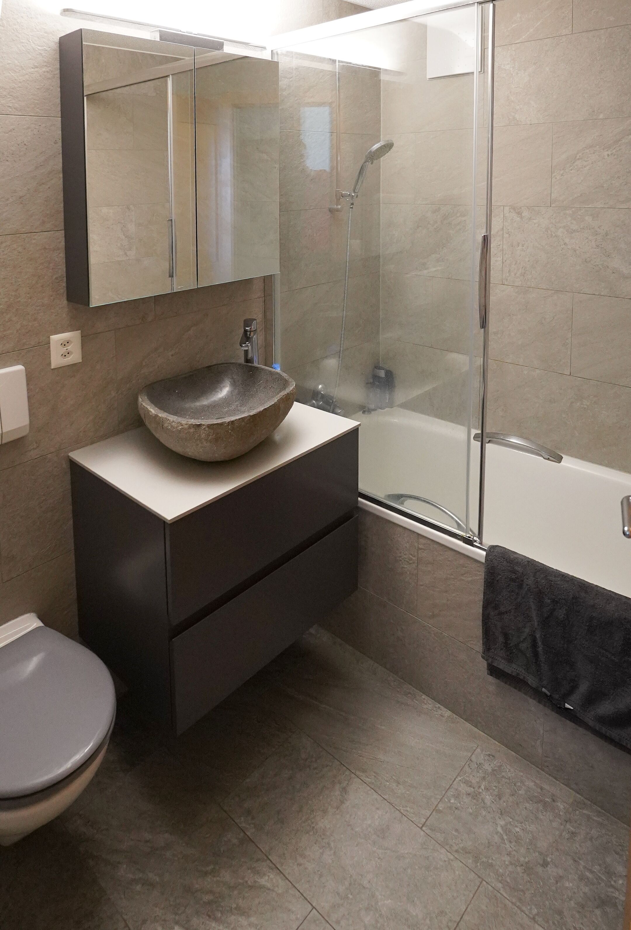 A modern bathroom with a glass-enclosed shower, a stone sink, and a dark vanity.