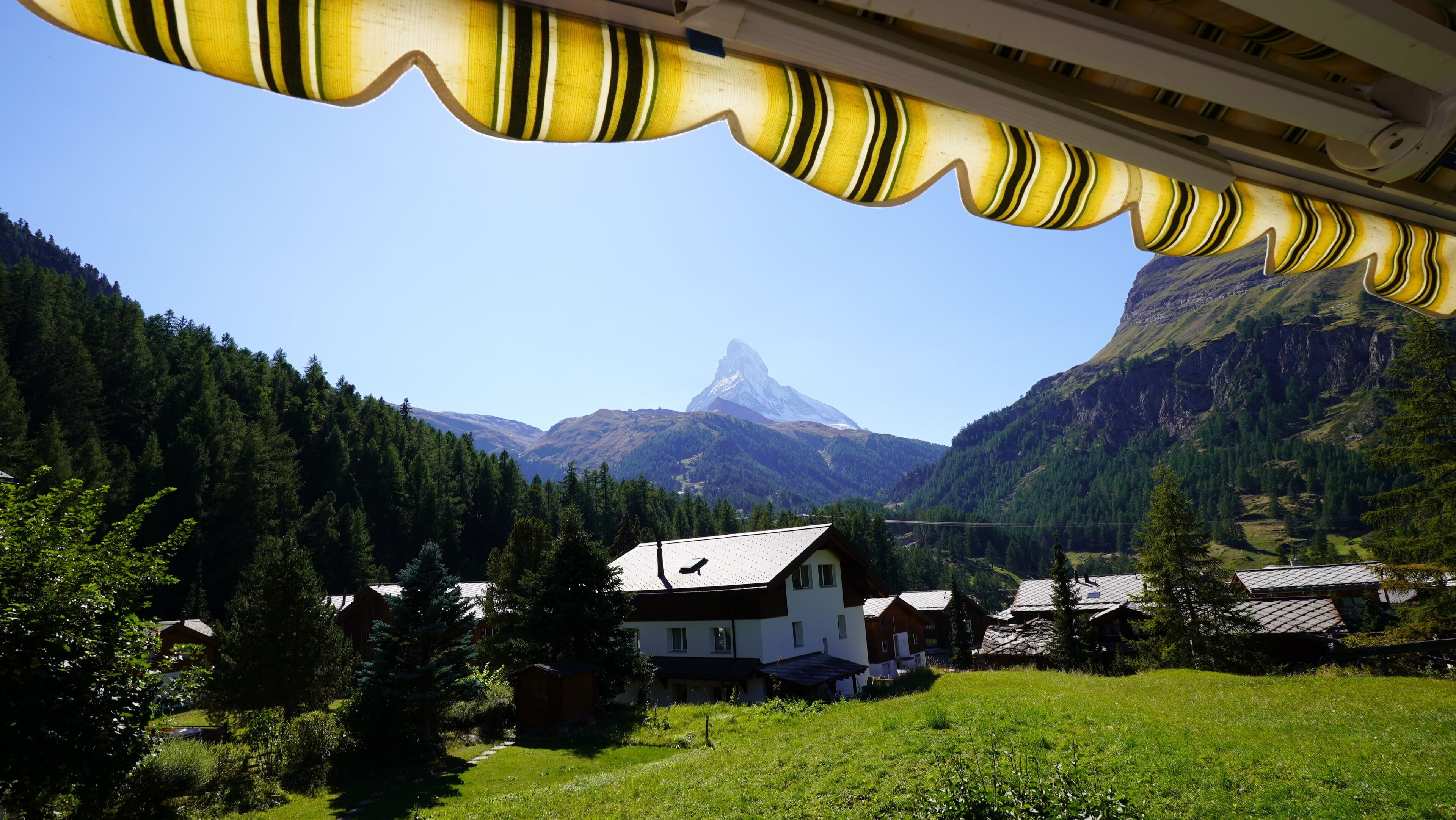 A mountain house with a view of a prominent peak, surrounded by forested hills.