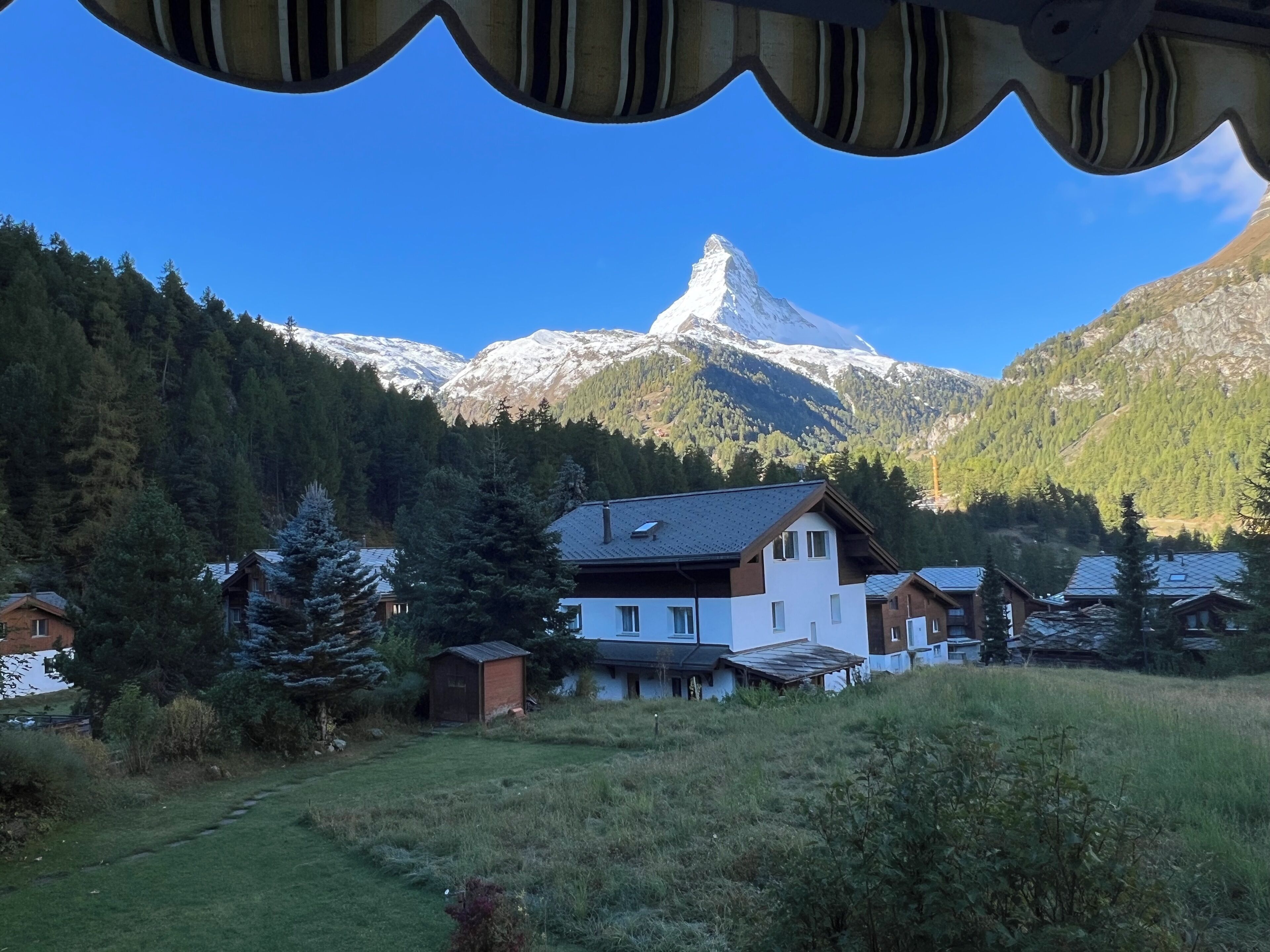 Una casa de montaña con vista a un pico nevado, rodeada de colinas boscosas.