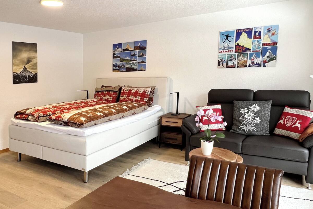 A modern bedroom with a bed, a sofa, a coffee table, and a wall with posters.