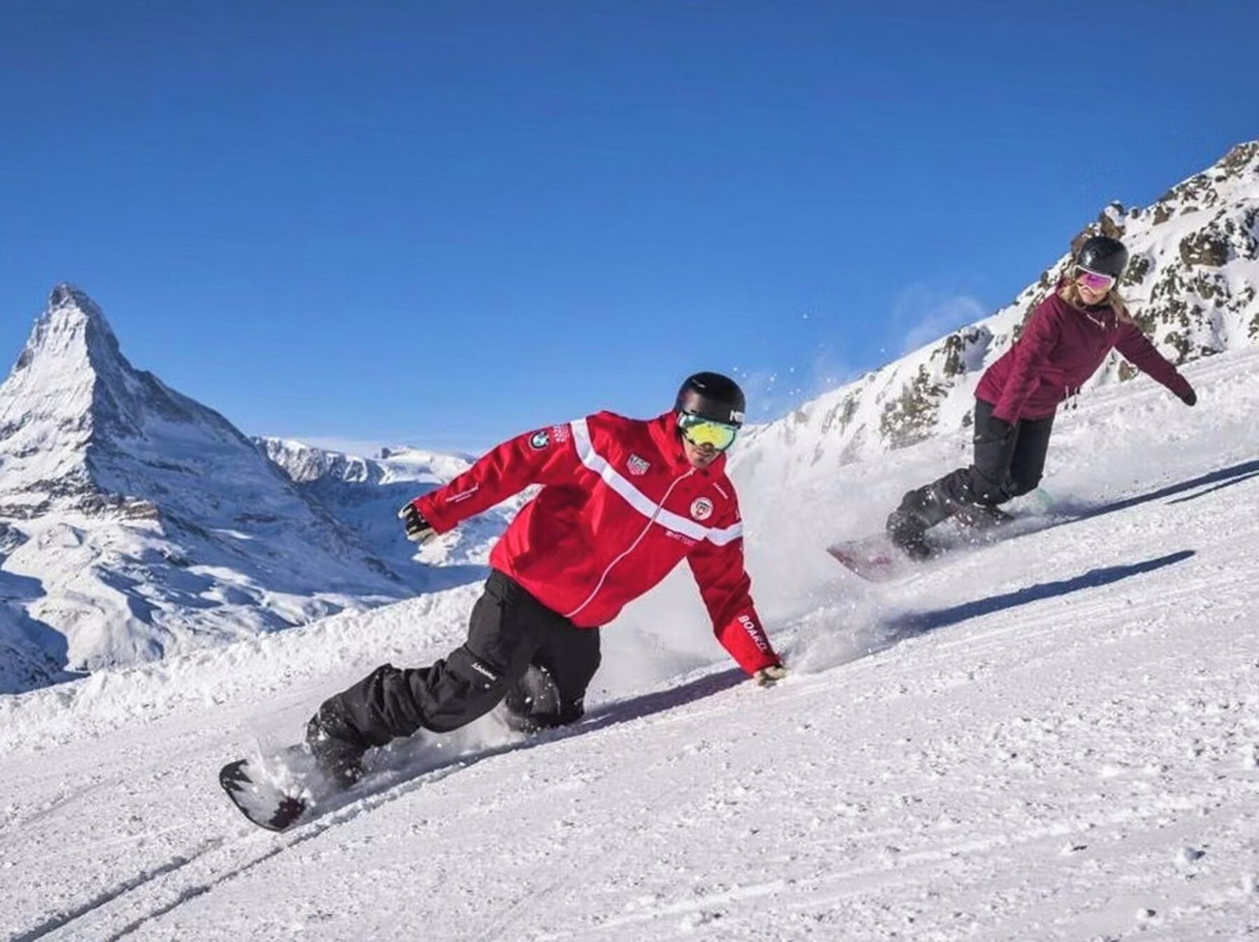 A snowy mountain slope with two skiers.