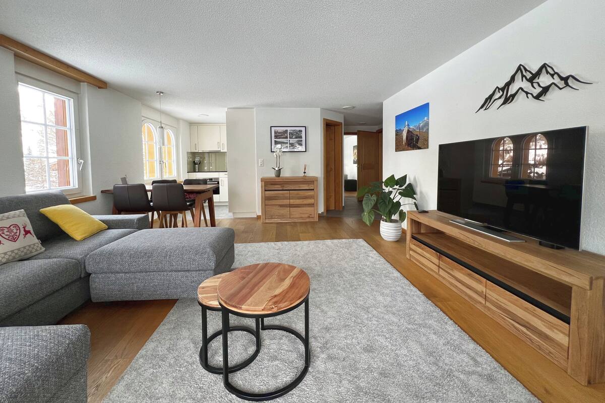 A modern living room with a grey sectional sofa, a wooden coffee table, and a flat-screen TV.