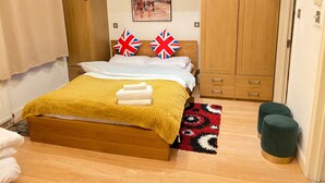 A bedroom with a wooden bed, two pillows with Union Jack designs, a yellow blanket, and a red and black patterned rug. - Stunning 1-bed Apartment in London (London)