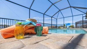 Un espace aménagé au bord de la piscine, avec un récipient en verre, une paille, un chapeau et une serviette.