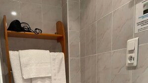 A small bathroom with a toilet, a shelf with towels, and a toilet paper holder. - N.D. Auxiliatrice (Lourdes)