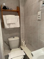 Un baño pequeño con inodoro, un estante con toallas y un dispensador de papel higiénico.
