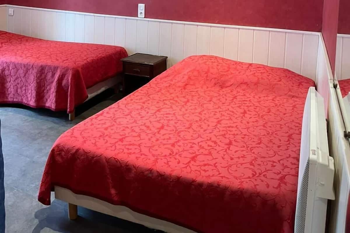 Quarto de hotel com duas camas de solteiro, uma pequena mesa de cabeceira, luminária na parede e radiador branco.