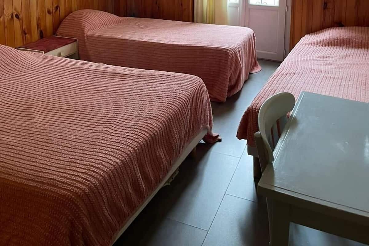 Quarto com duas camas, uma mesa, uma cadeira, um quadro na parede e uma janela com cortinas.