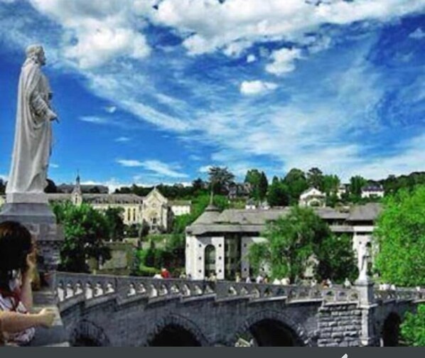 Un puente de piedra con una estatua a la izquierda, un cielo azul despejado y edificios al fondo.